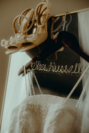Bridal details featuring pearl heels, a Mrs. Russell hanger, lace wedding dress, and veil in warm light.