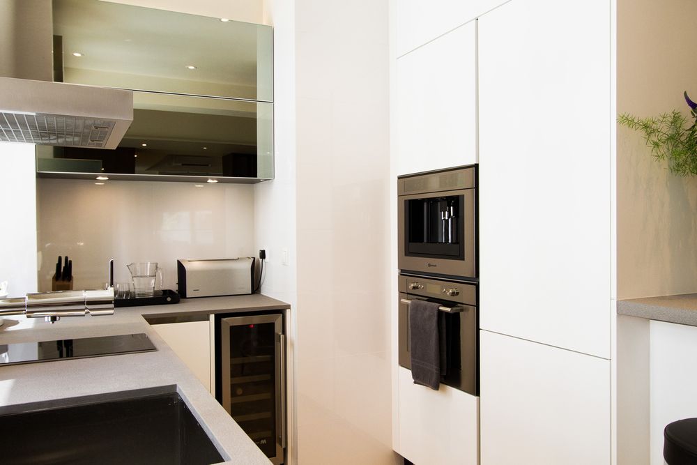 Minimalist white kitchen with built-in oven, wine cooler, stainless steel hood, and sleek cabinetry.