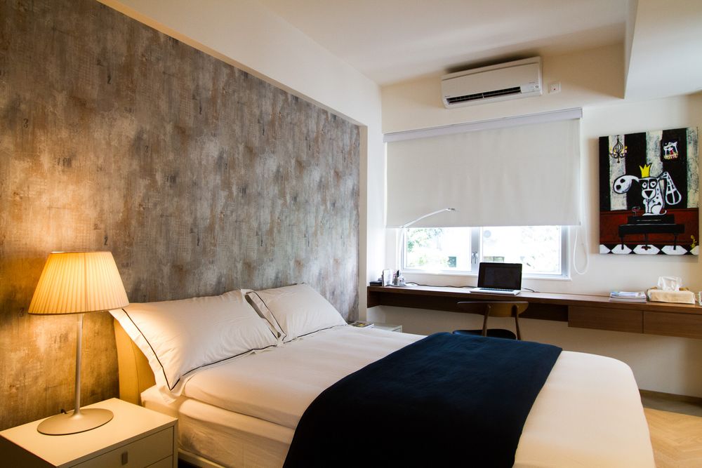 Contemporary bedroom featuring a concrete textured headboard wall, double bed with navy throw, and built-in wooden desk by window.