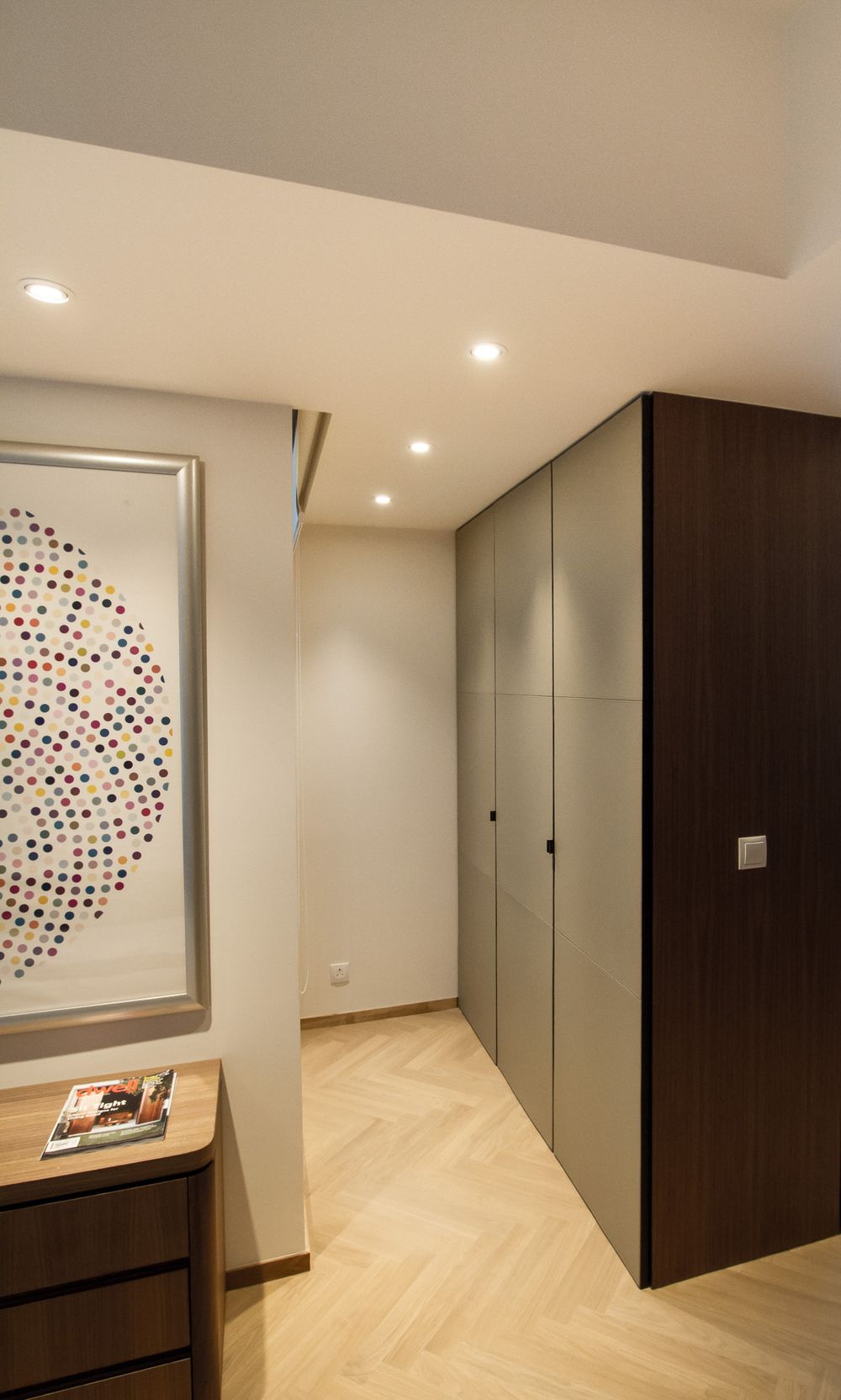 Modern hallway with herringbone parquet flooring, built-in wardrobe cabinets, and colorful dot artwork on white wall.
