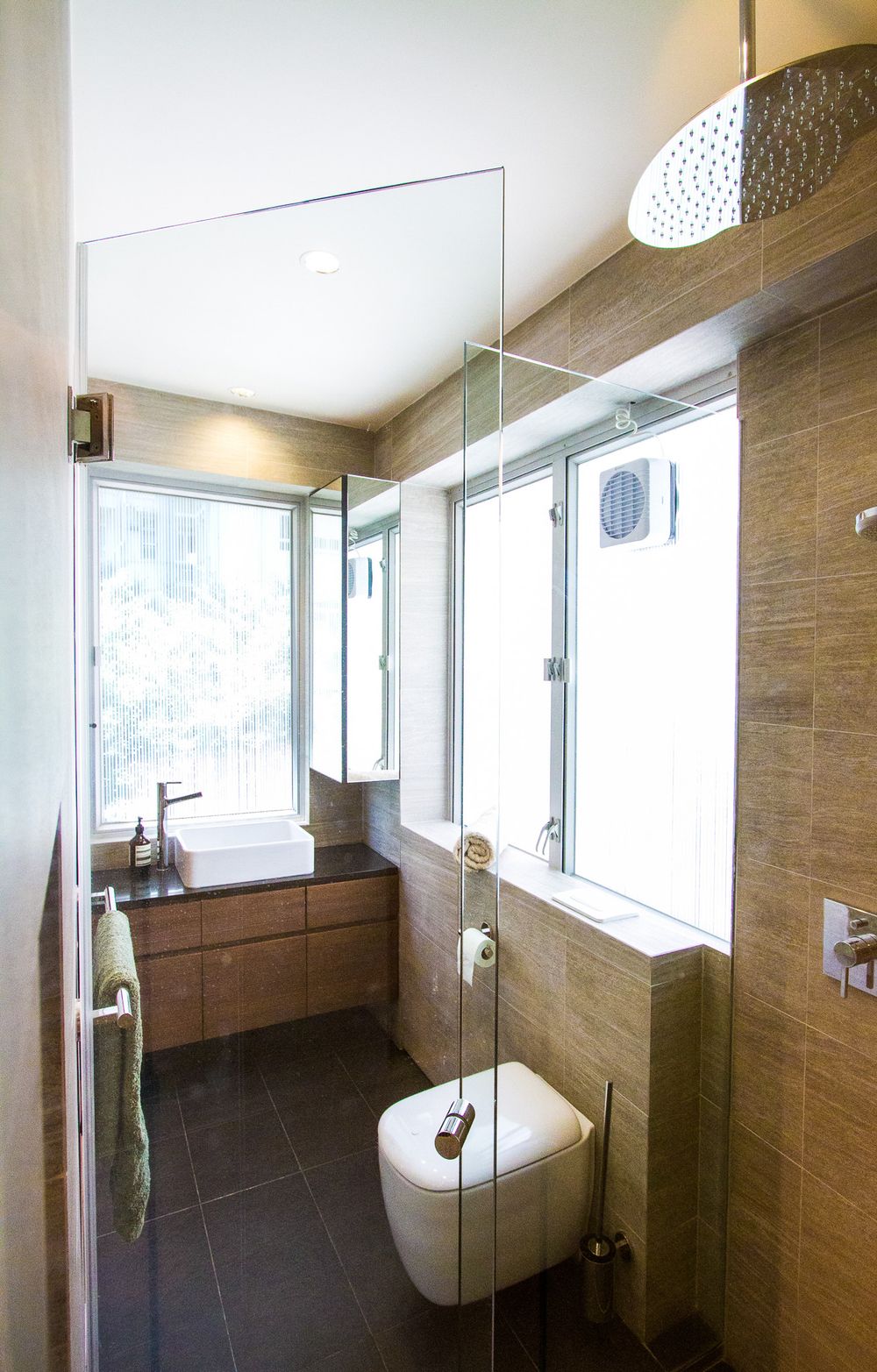 Compact modern bathroom with wood-effect tiles, wall-hung toilet, glass shower enclosure, and rain shower head.