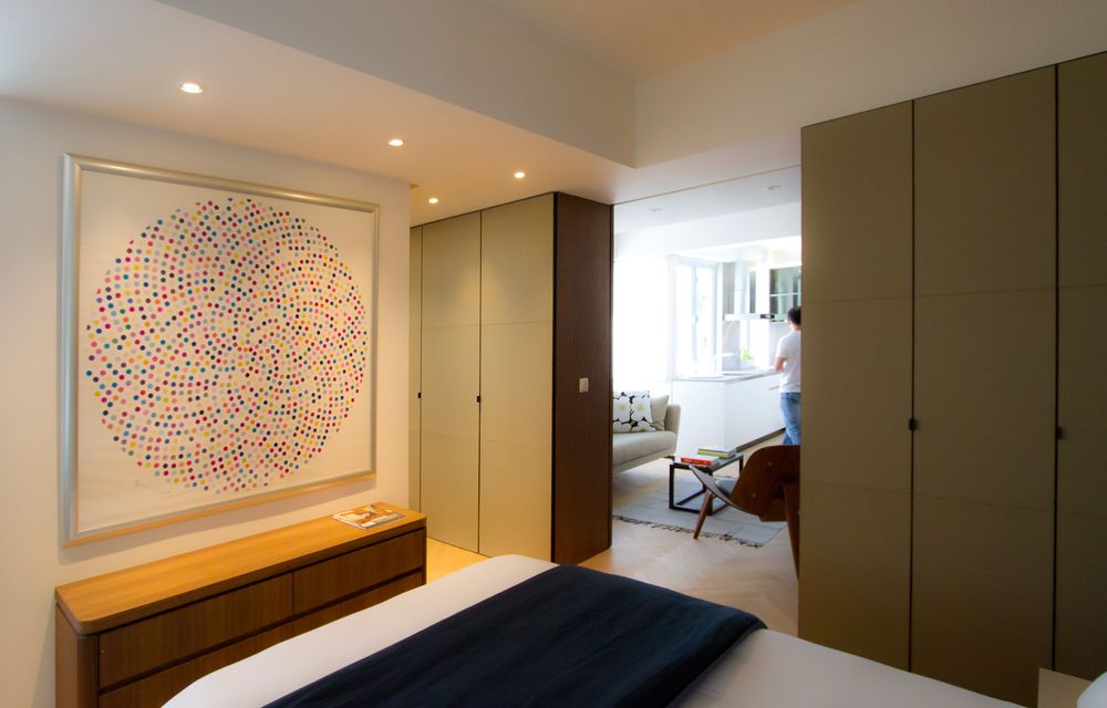 Elegant bedroom with large circular dot artwork, olive green built-in wardrobes, and wooden sideboard with navy bedding.