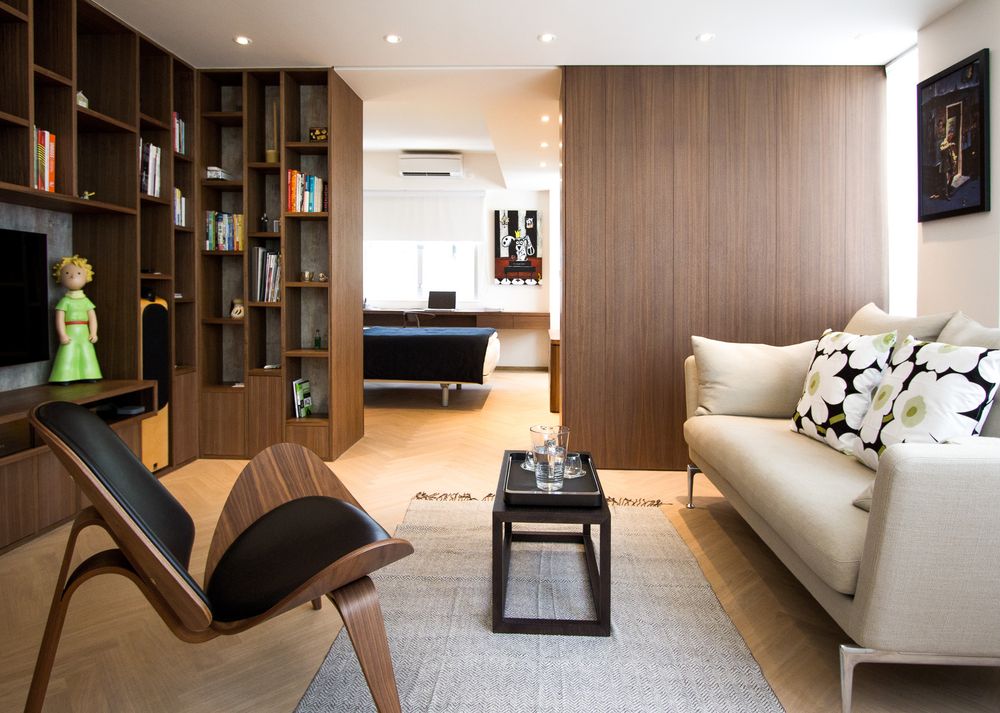 Stylish living room with walnut bookcase, cream sofa with Marimekko cushions, leather chair, and wooden panel wall.