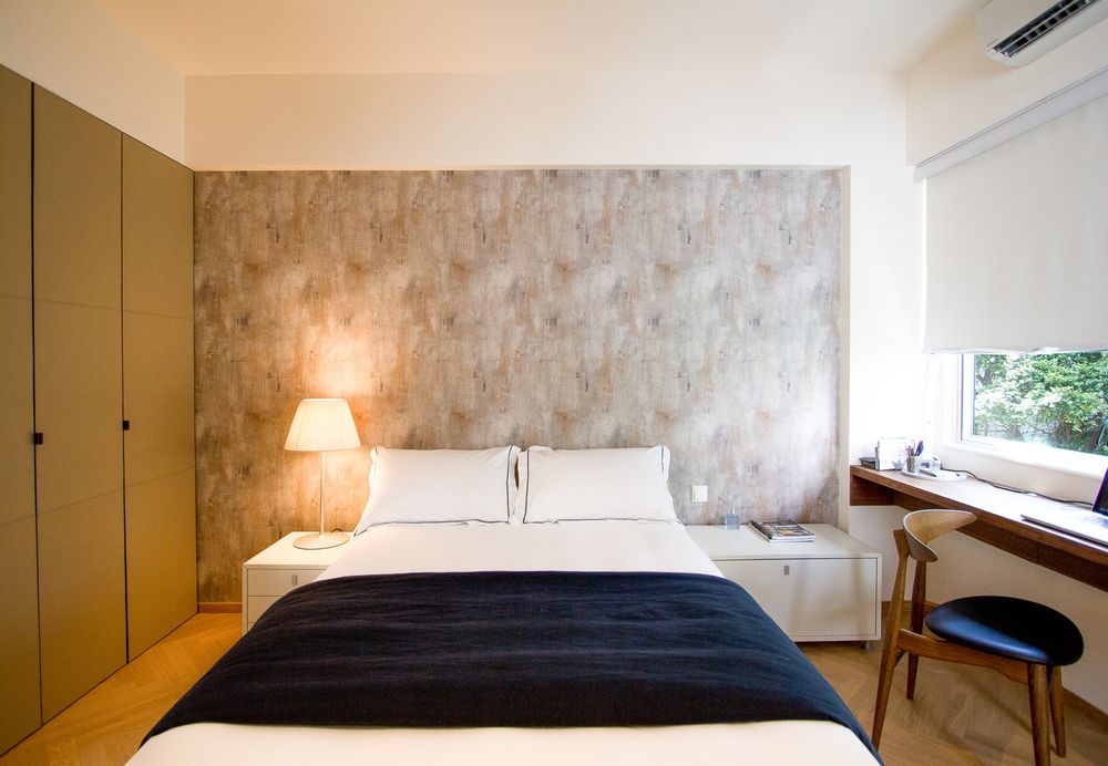 Serene bedroom with textured stone-effect feature wall, white bedding, navy throw, bedside lamp, and window desk.