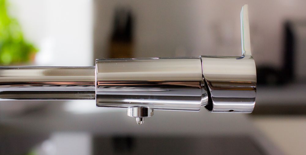 Close-up of a modern chrome kitchen faucet with a sleek single-handle design on a dark countertop.