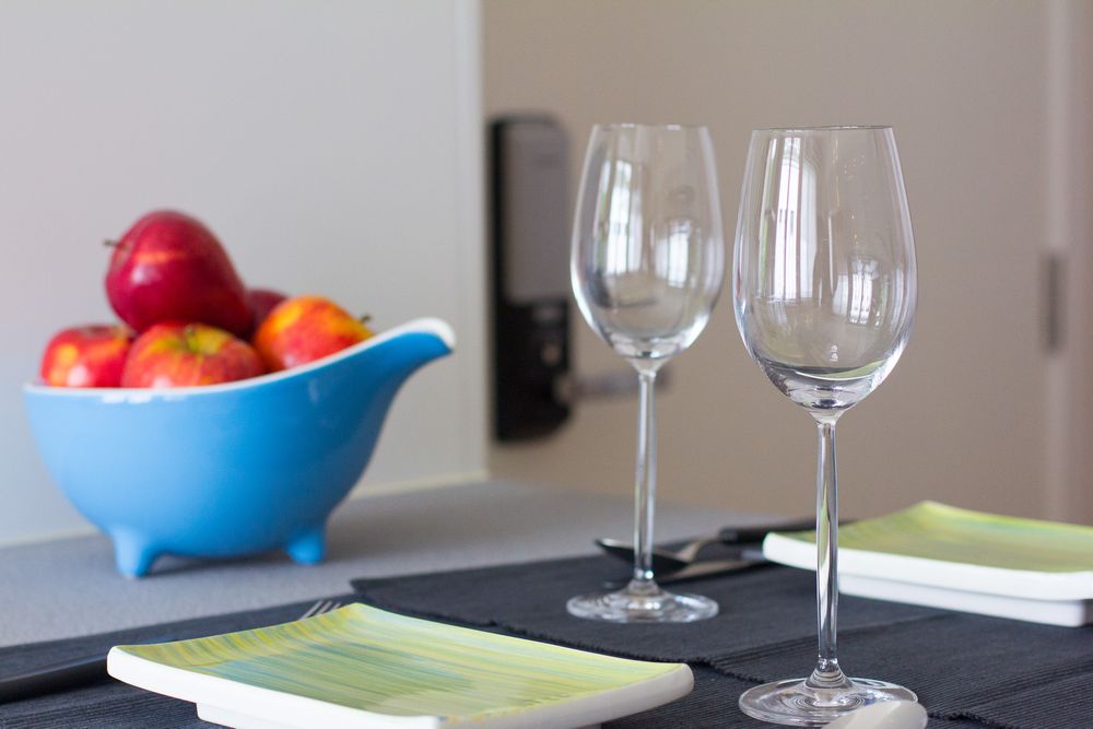 Two elegant wine glasses on a dark table with a blue bowl of red apples in the background.