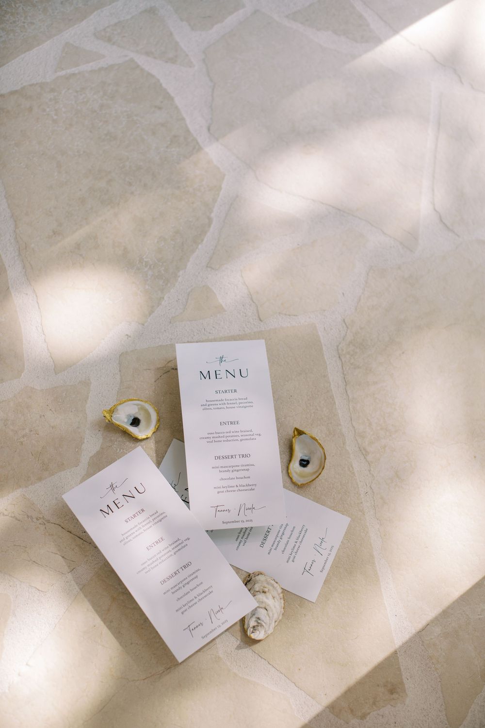 Elegant wedding menu cards displayed on marble surface with decorative shells and golden accents in natural light.