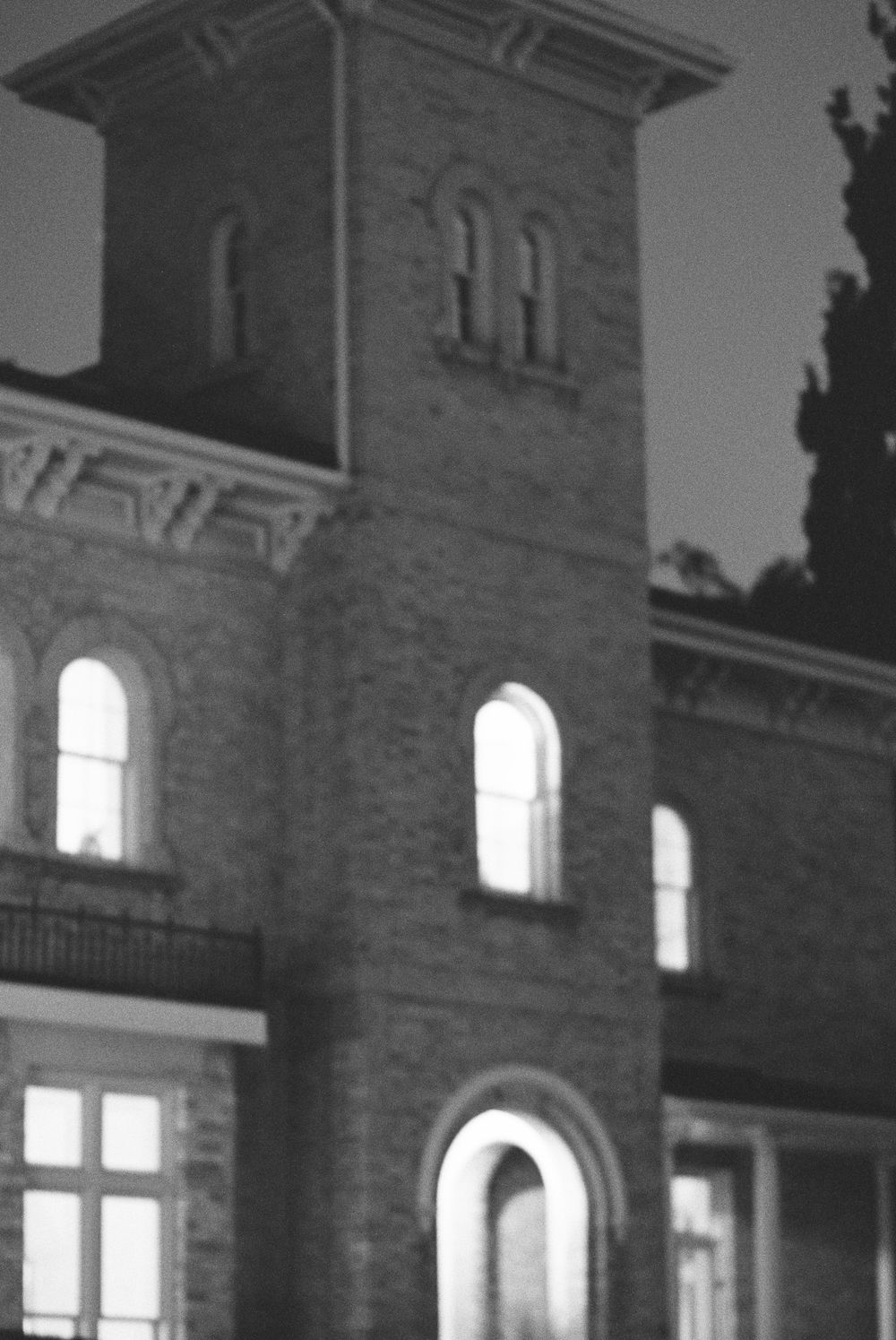 Black and white photo of a historic brick building at night with illuminated arched windows and a tower.