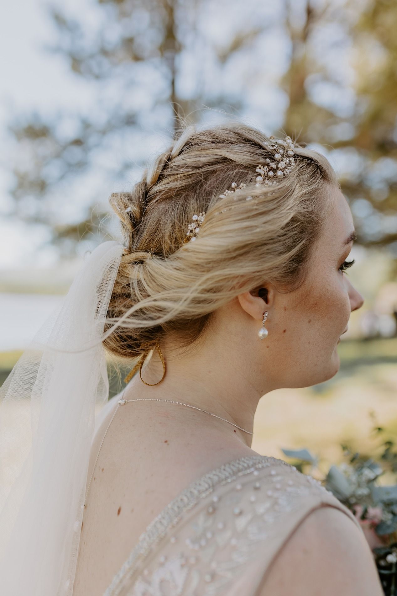 Smiling bride in lace gown holding floral bouquet with eucalyptus outdoors among pine trees on her wedding day at Lake Cuyamaca, Julian.
