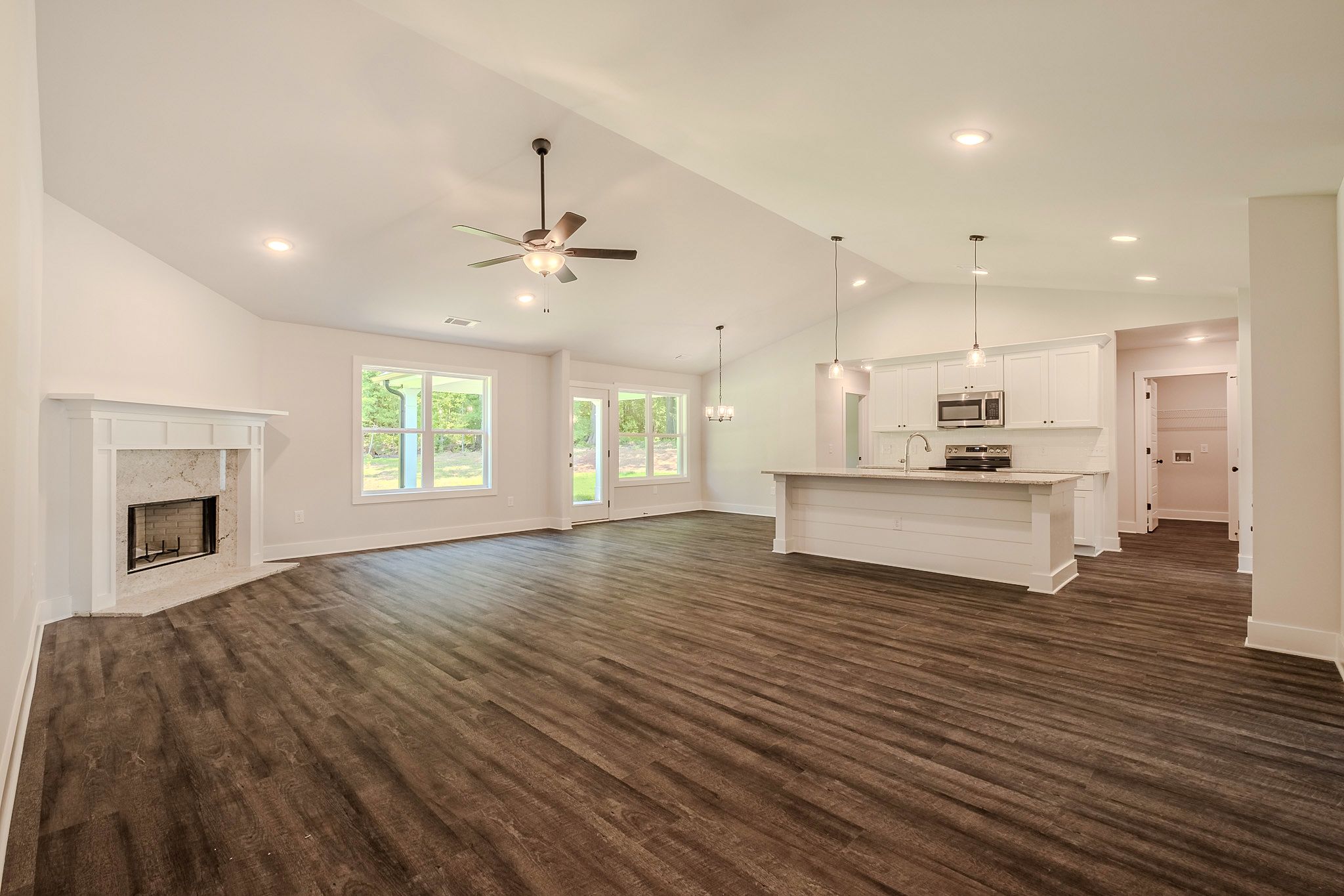 Open-concept living room with dark hardwood floors, vaulted ceiling, fireplace, and modern kitchen with island and pendant lights.