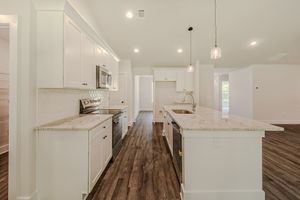 Modern kitchen with white cabinets, granite island, stainless appliances, pendant lights, and dark hardwood floors.