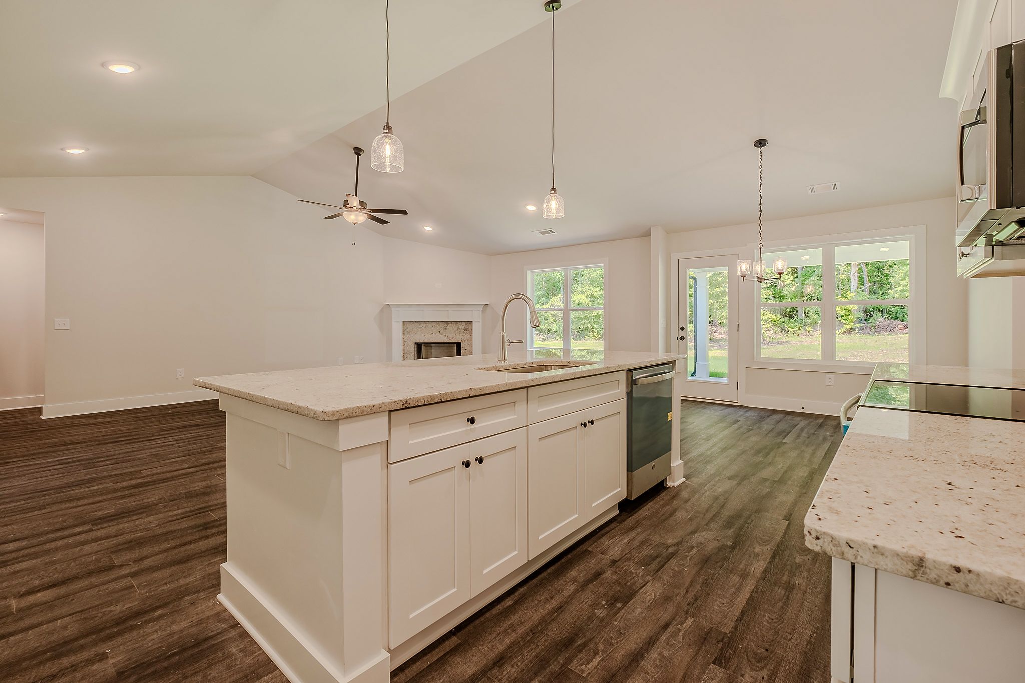 Modern kitchen with white cabinets, granite countertops, dark hardwood floors, and pendant lights over a large island.