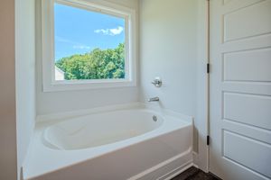 White soaking bathtub beside a bright window with green tree views in a clean modern bathroom.