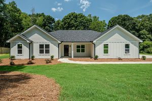 Modern ranch-style home with gray siding, black roof, manicured lawn, and lush green trees in the background.