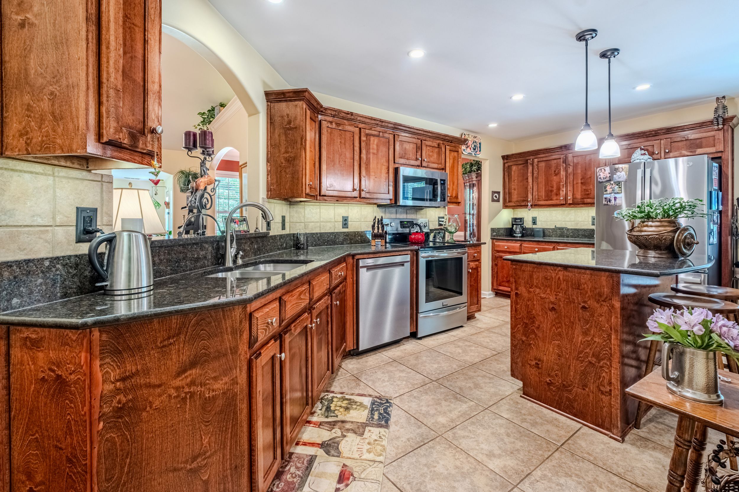 Spacious kitchen with rich cherry wood cabinets, dark granite countertops, stainless steel appliances, and elegant pendant lighting.