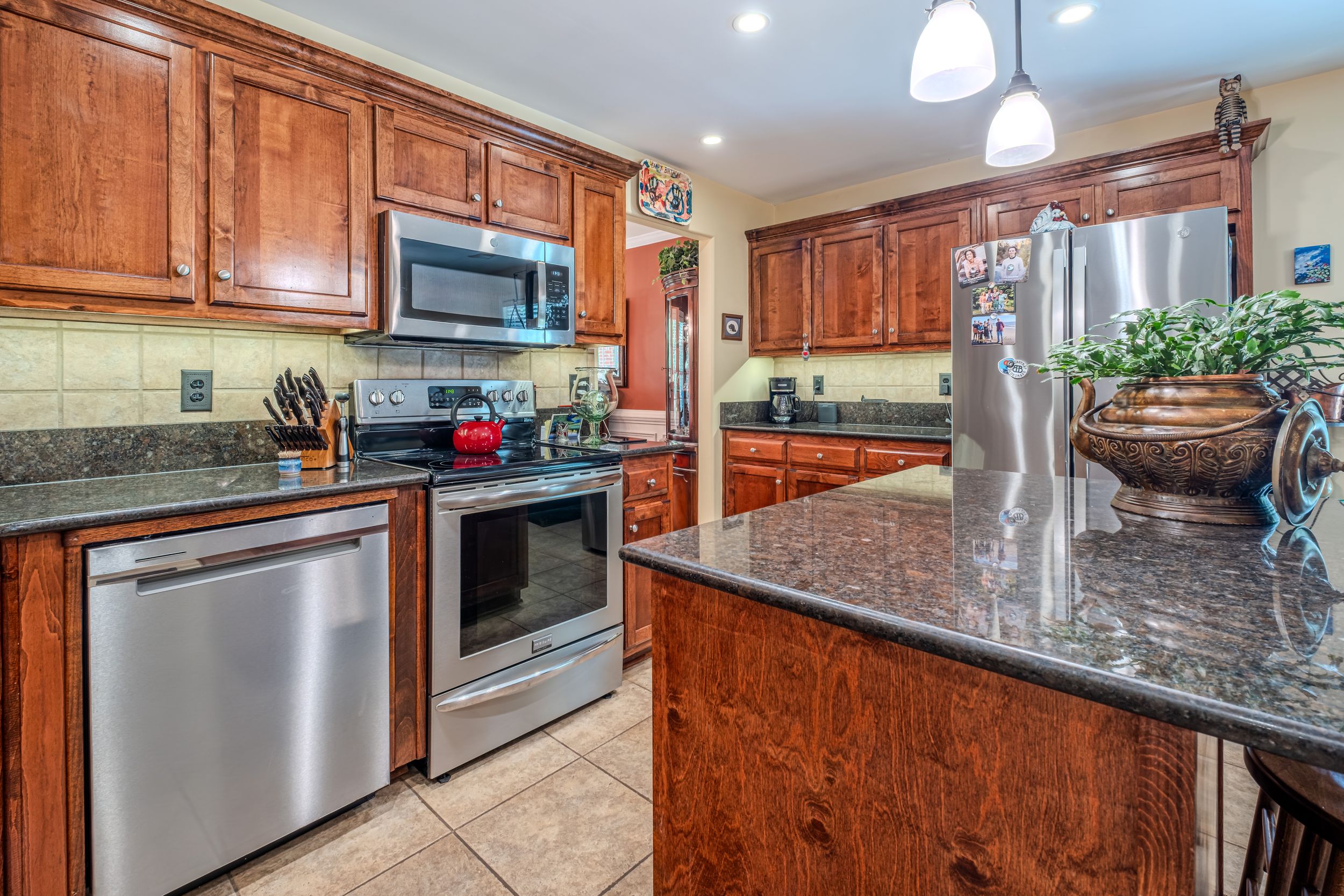 Modern kitchen with stainless steel appliances, dark granite countertops, and rich wood cabinetry on tile flooring.