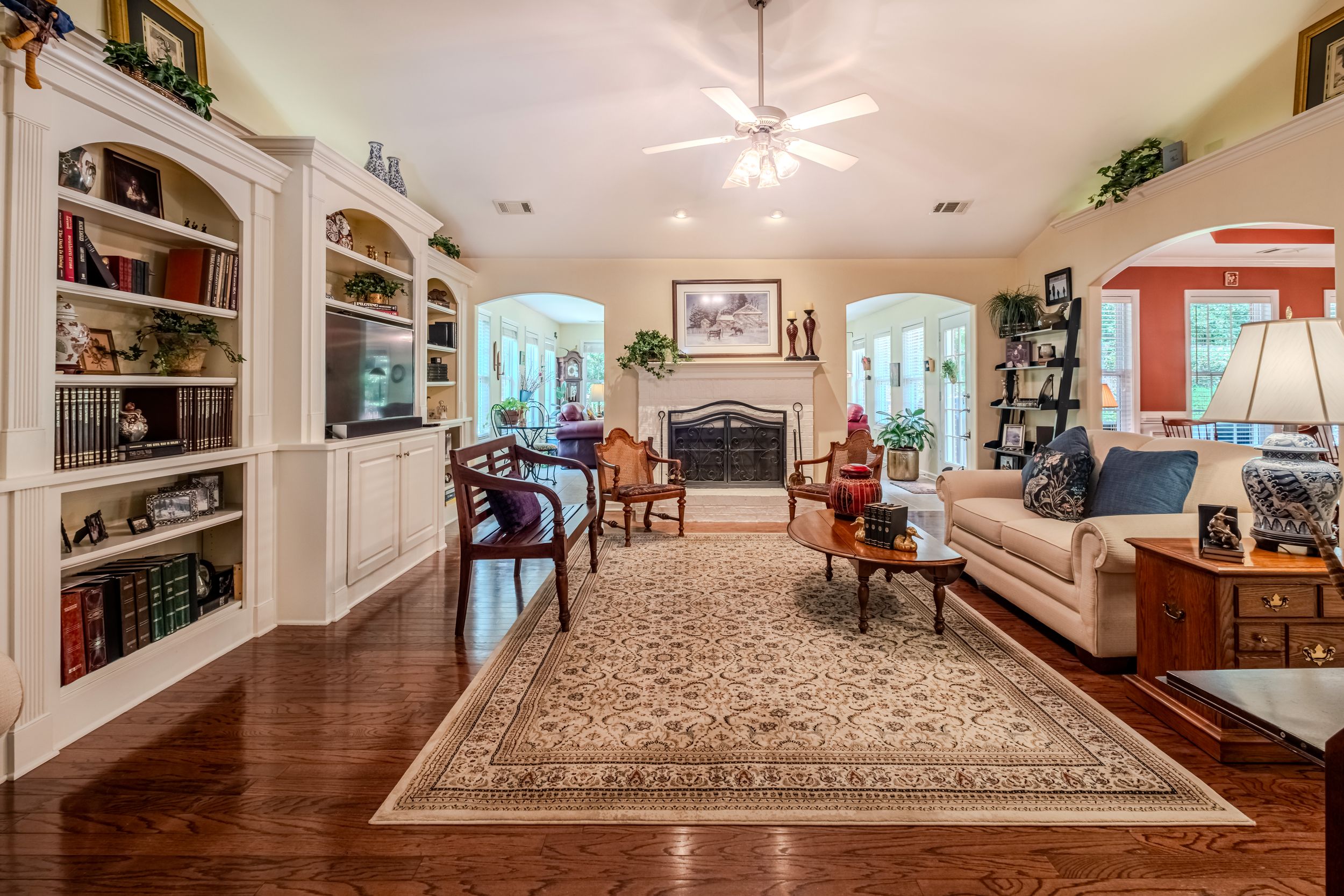 Elegant living room with hardwood floors, built-in bookshelves, fireplace, arched doorways, and a large area rug.