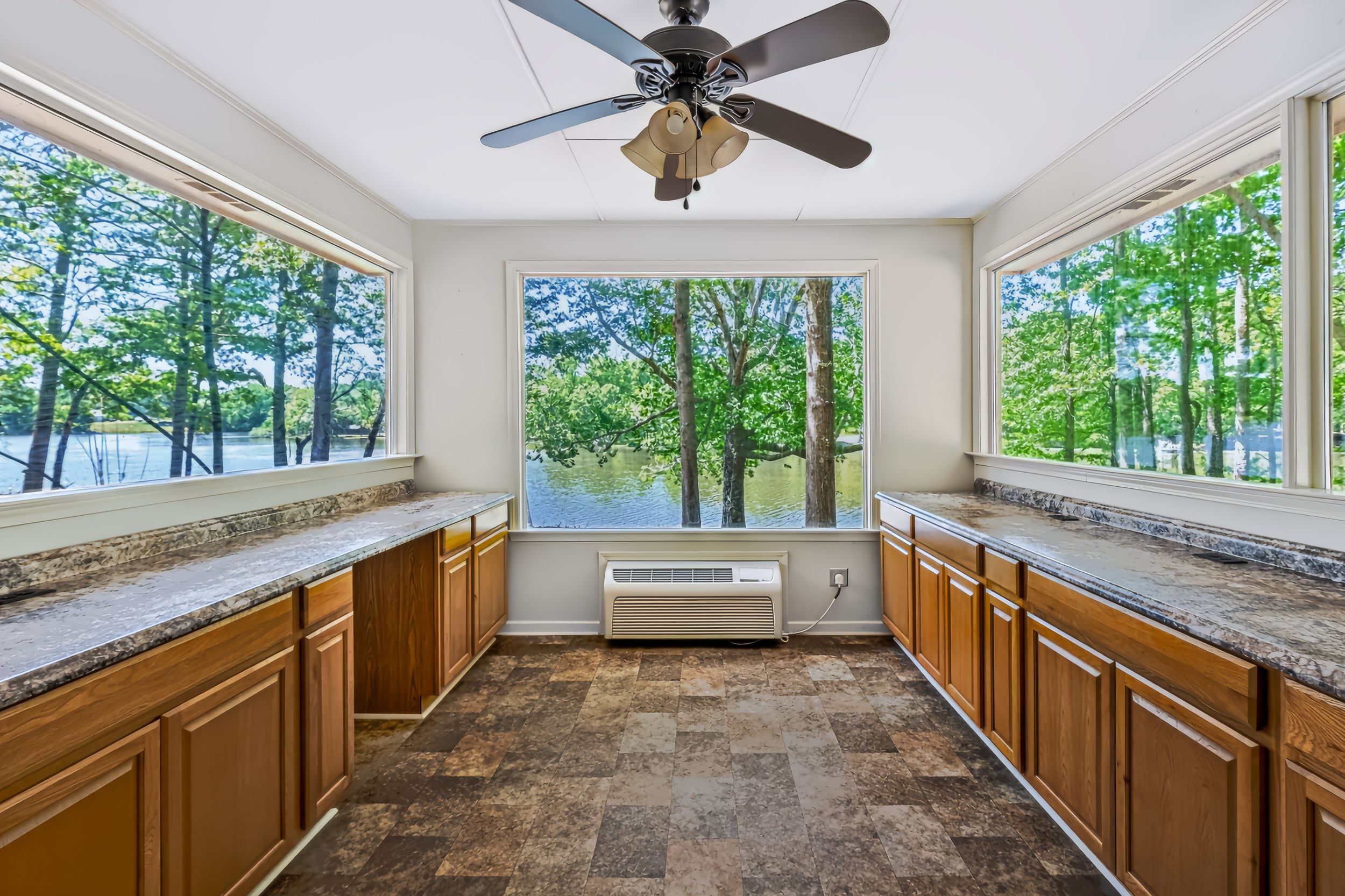 Spacious kitchen with granite countertops, oak cabinets, stone tile floors, and large windows overlooking a serene lakeside forest view.