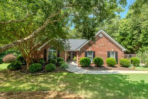 Brick ranch home with lush green lawn, mature trees, manicured shrubs, black shutters, and charming curb appeal.