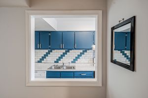 Modern kitchen with blue cabinets, white subway tile backsplash, and stainless steel sink viewed through a window frame.