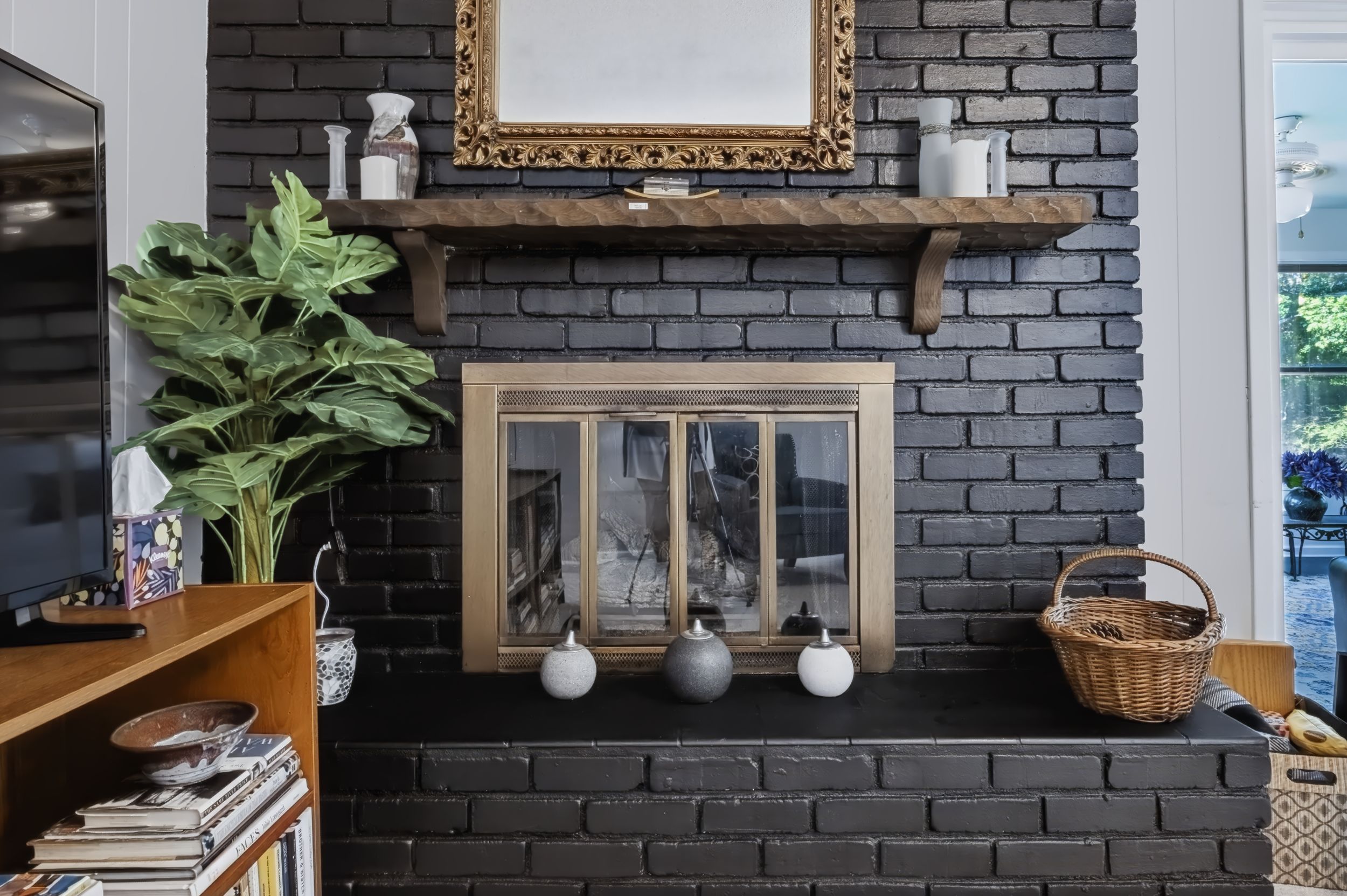 Black painted brick fireplace with gold mirror, wooden mantel shelf, brass fireplace doors, and decorative vases.