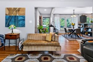 Bright open-concept living room with striped sofa, Tiffany lamp, hardwood floors, and dining area with chandelier in background.