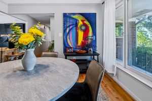 Dining area with round stone table, leather chairs, yellow flowers, and a vibrant large abstract painting on the wall.
