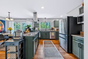 Modern kitchen with green cabinets, granite island, stainless steel appliances, and hardwood floors.