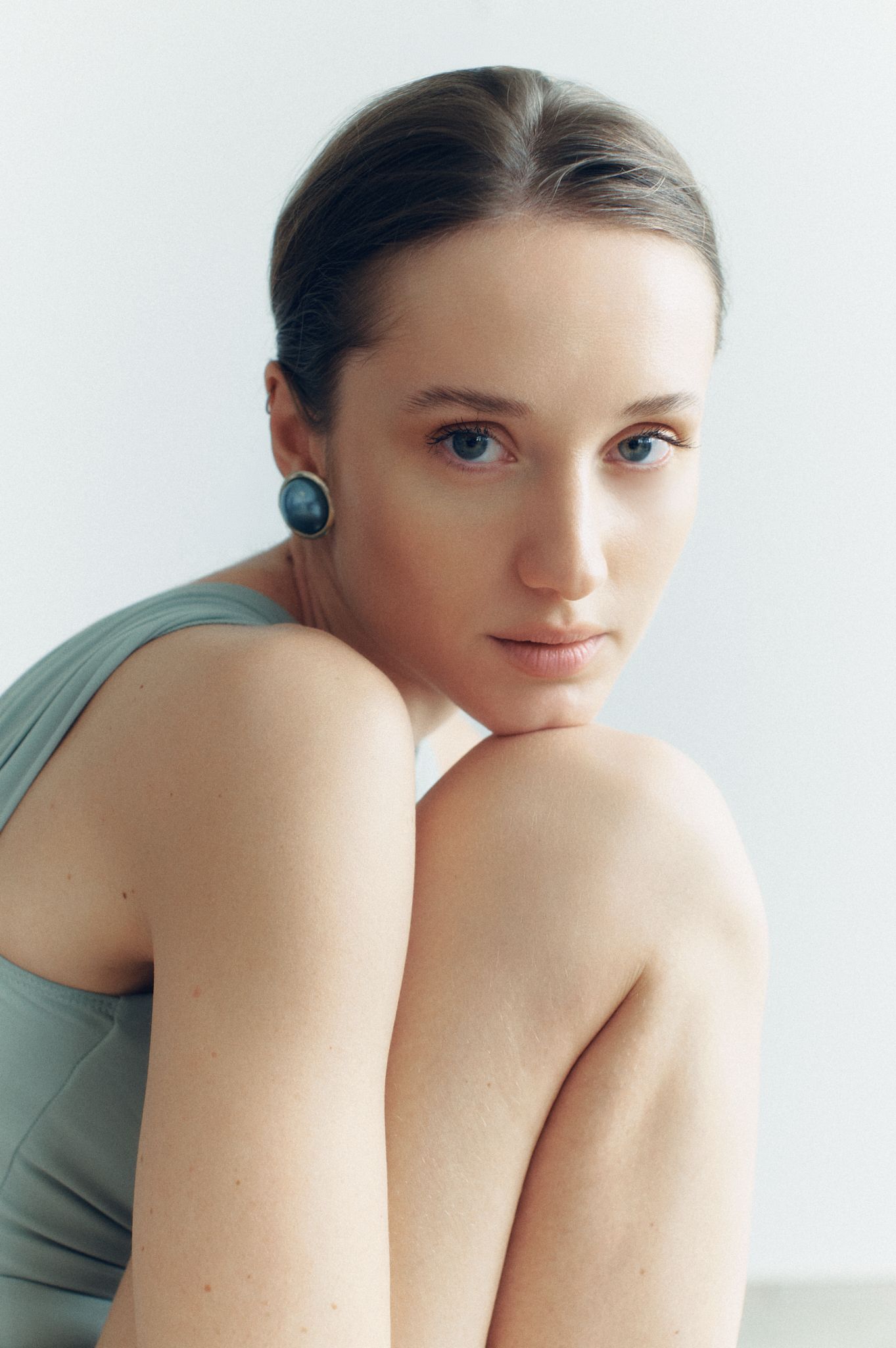 Young woman wearing gold geometric triangle ear cuff earrings, minimalist jewelry portrait on white background.