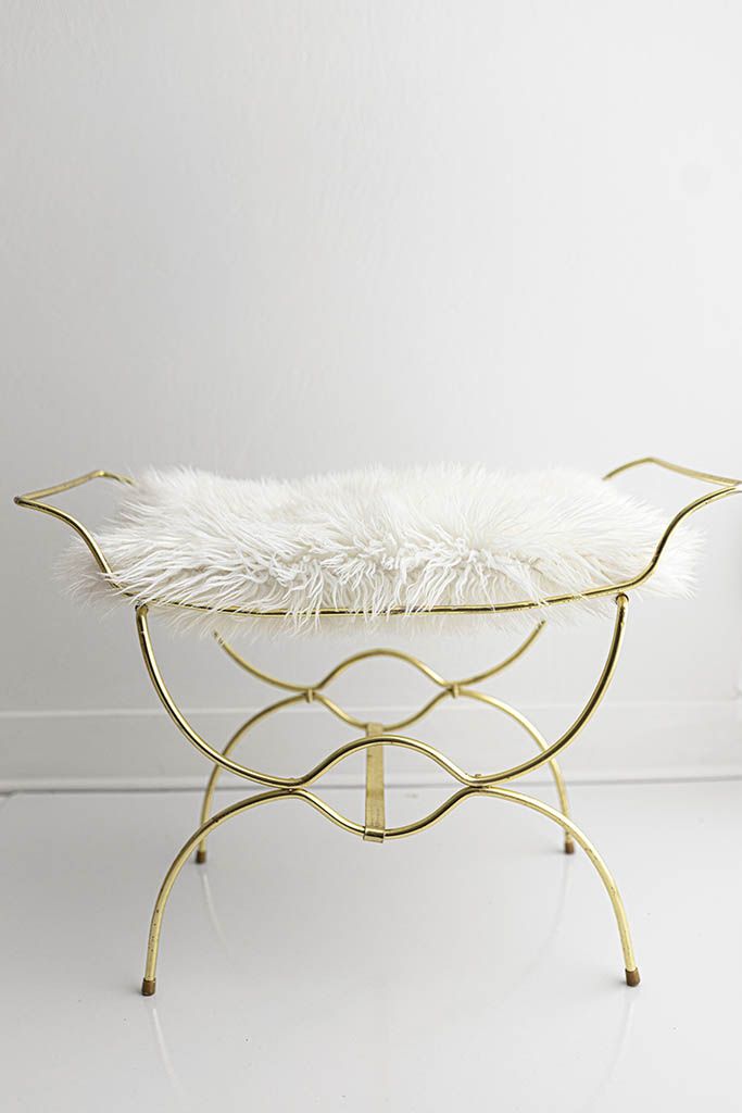 Gold metal vanity stool with ornate curved frame and plush white faux fur cushion seat.