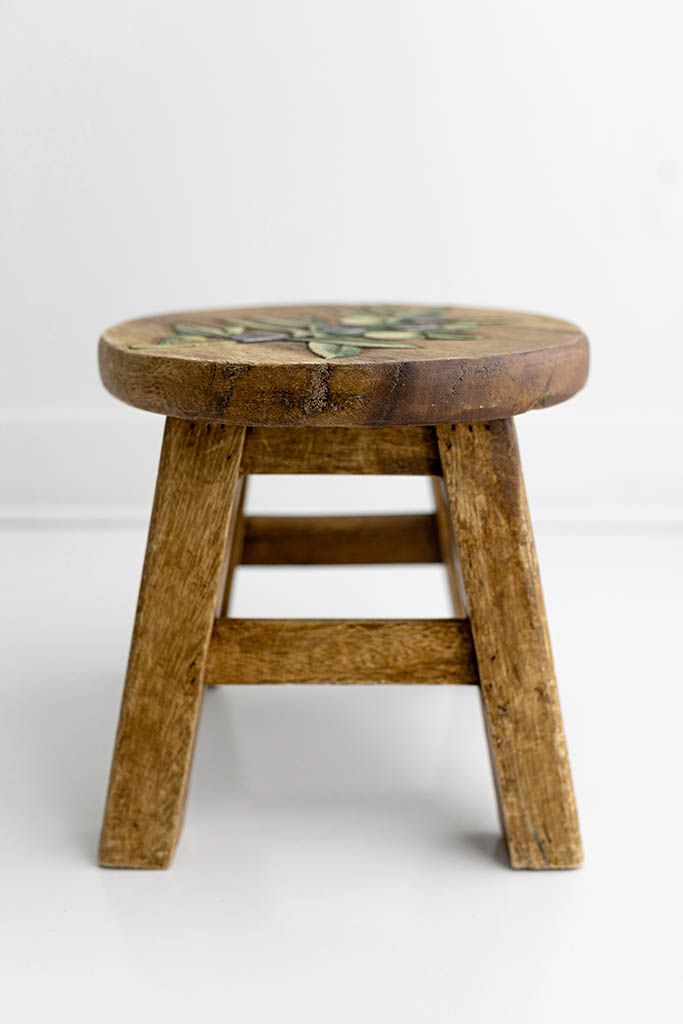 A small wooden stool with decorative painted floral top and four legs on white background.