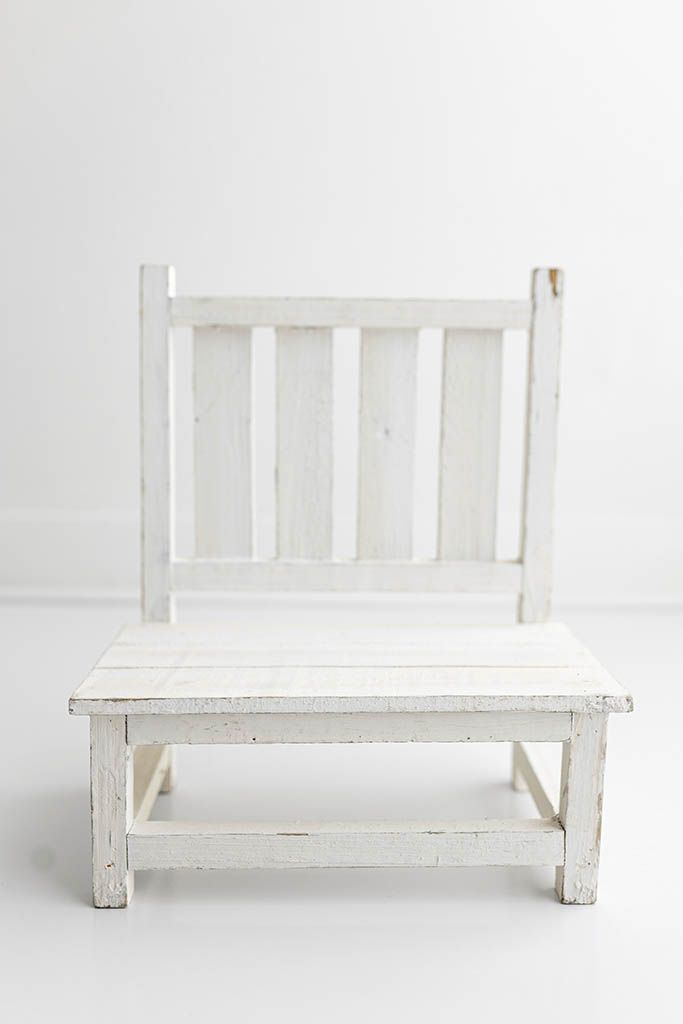 A rustic white painted wooden child's chair with slatted back on white background.