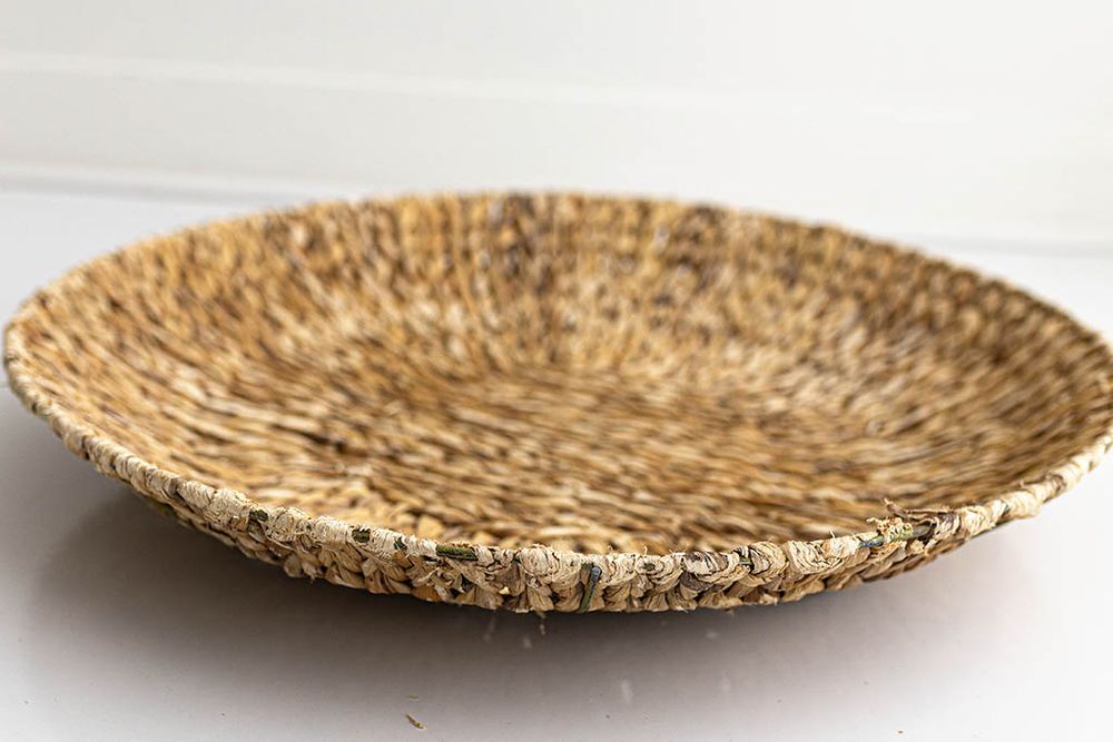 Flat round woven seagrass decorative bowl on white surface.