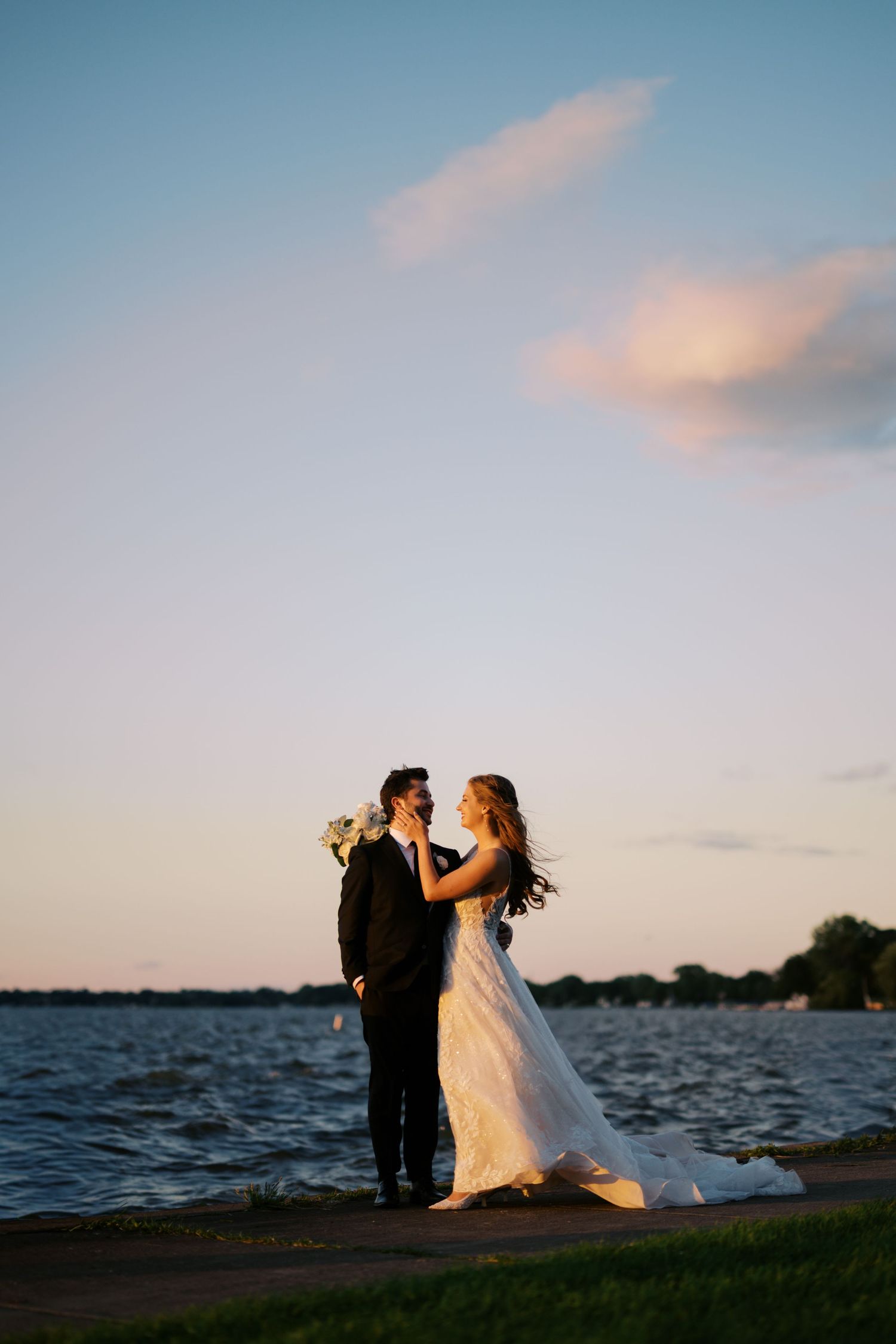 Bride and groom share a romantic moment by the waterfront at golden hour sunset.