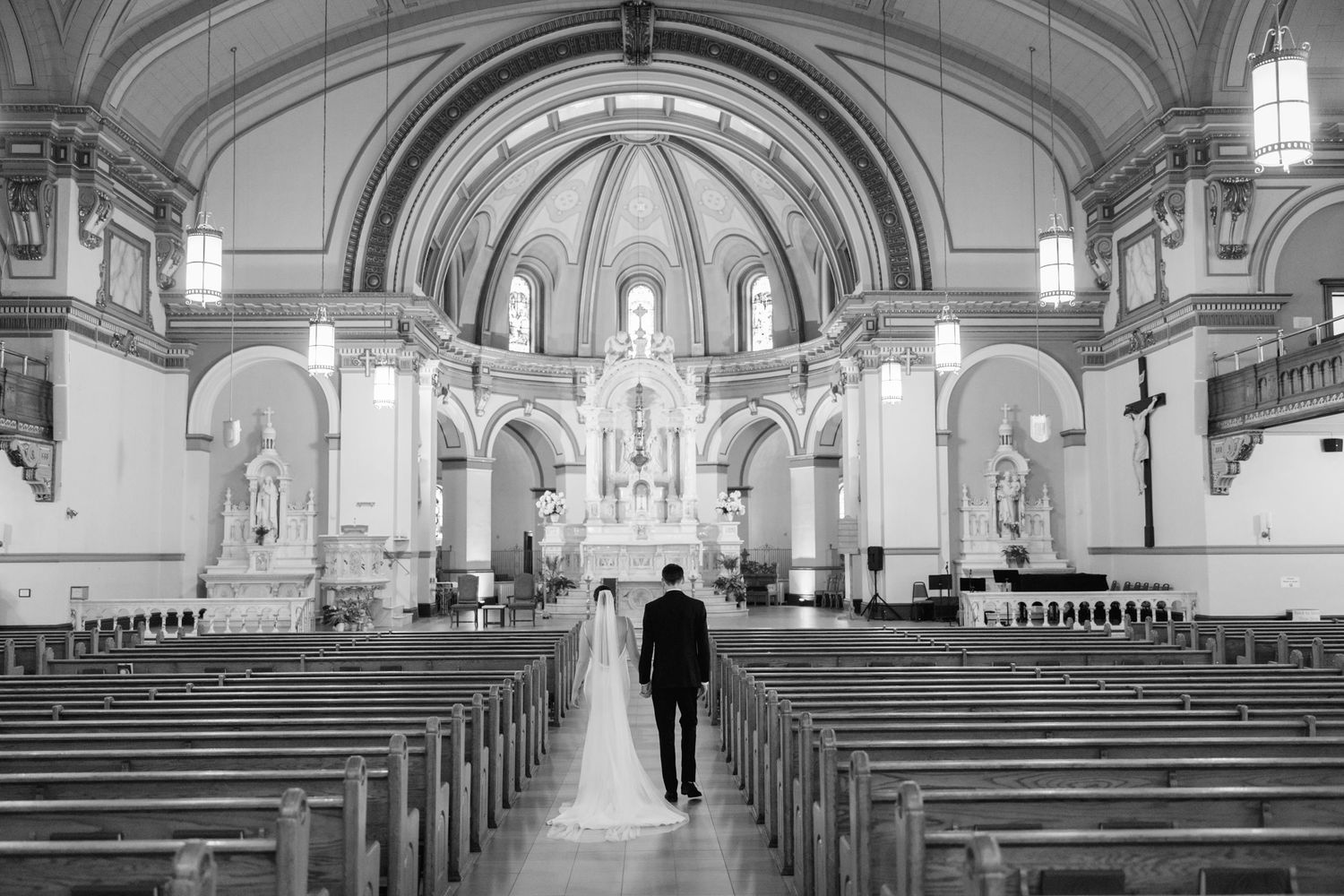 Black and white photo of a couple walking down a church aisle toward the altar on their wedding day.