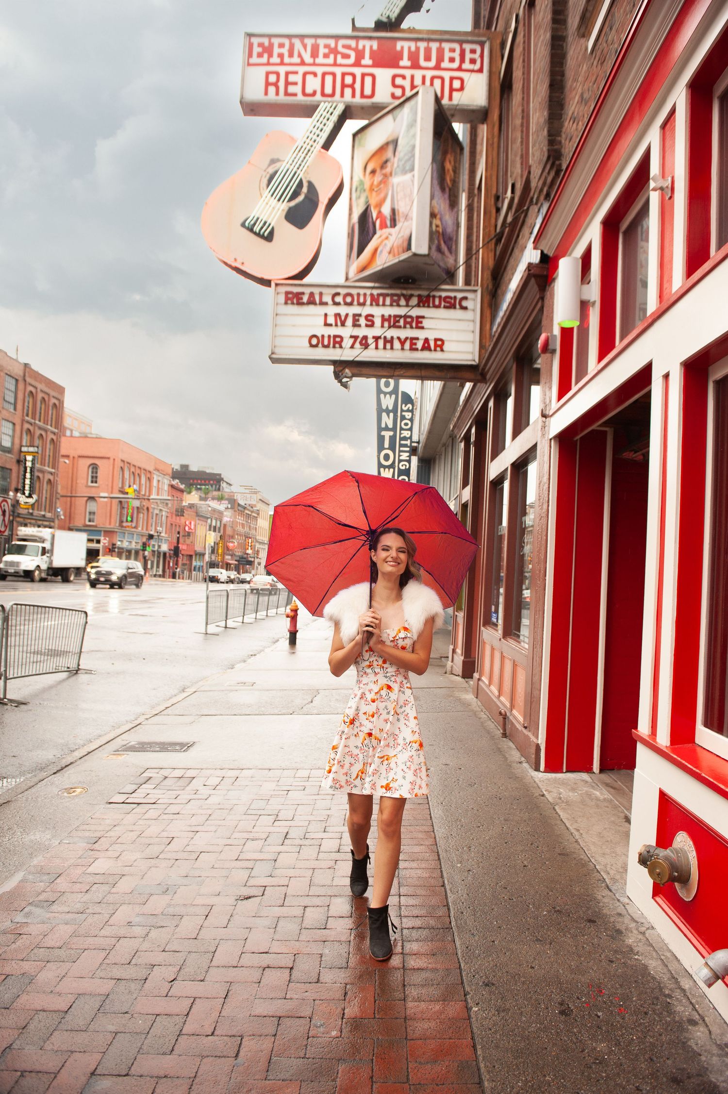 Woman with red umbrella walks past Ernest Tubb Record Shop on a rainy Nashville street.