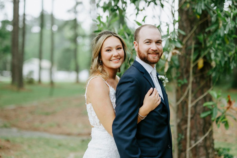 Bride and groom posing together outdoors near pine trees on their wedding day.