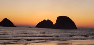Coastal sea stacks silhouetted against a warm orange sunset over the ocean