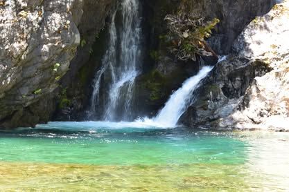 Small waterfall flowing into a clear turquoise pool surrounded by rocks and greenery