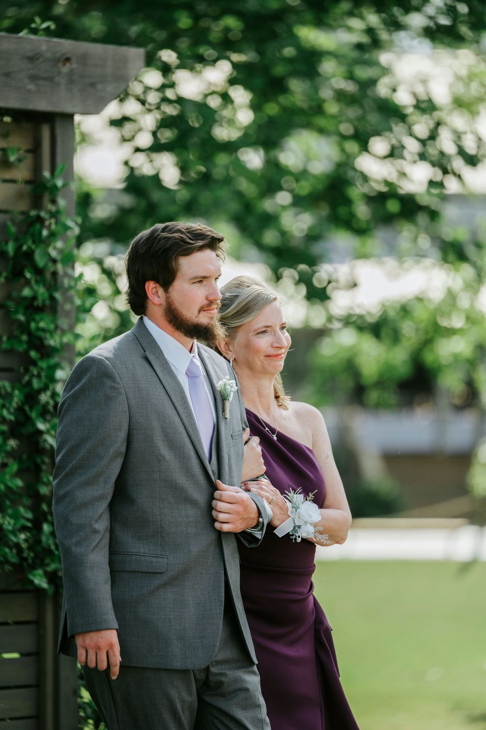Groomsman escorts woman in purple gown at outdoor wedding ceremony.