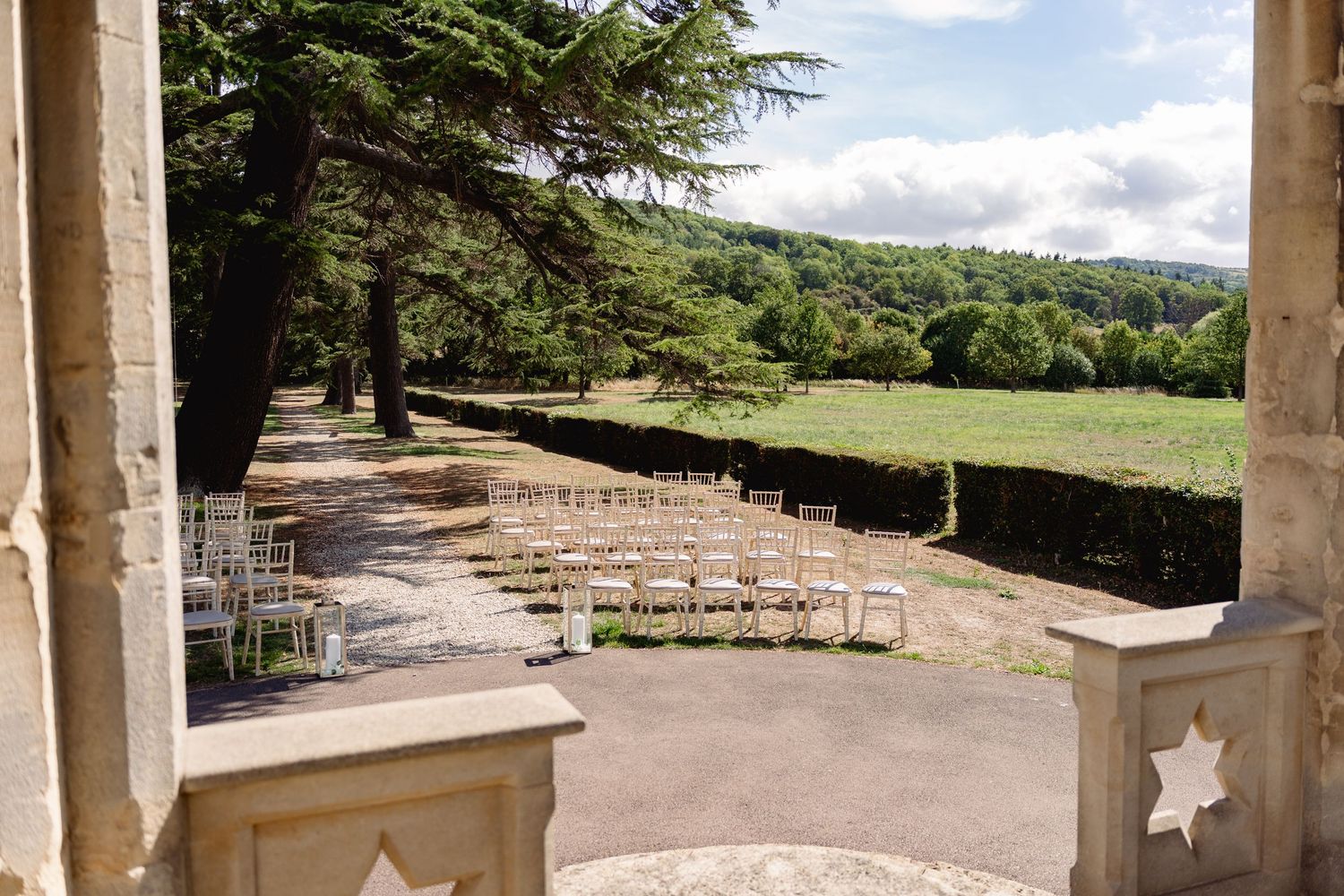 Elegant outdoor wedding ceremony setup with rows of chairs on a terrace overlooking lush green countryside.