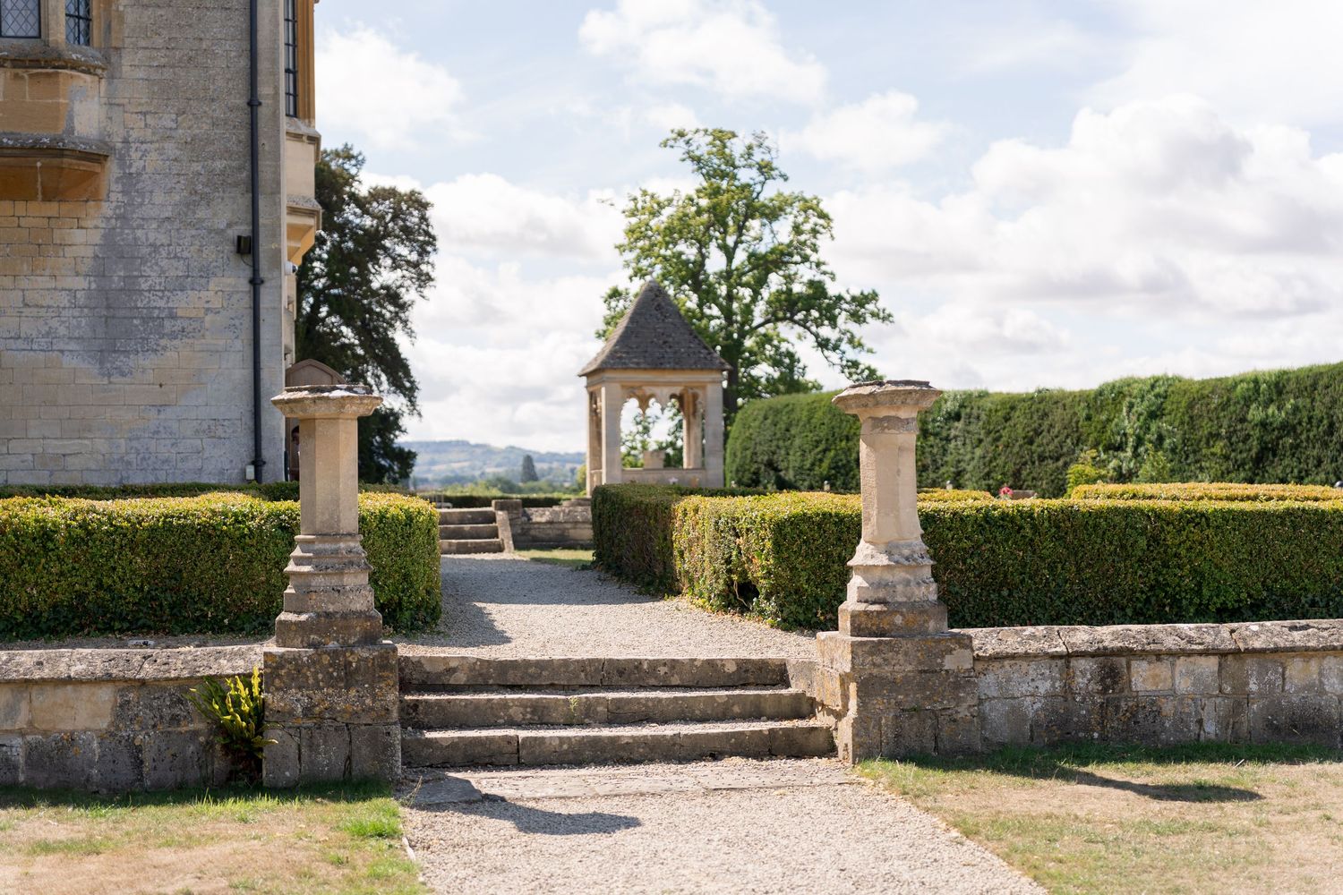Stone garden path with ornate gazebo, trimmed hedges, and classical pillars at a historic English country estate.