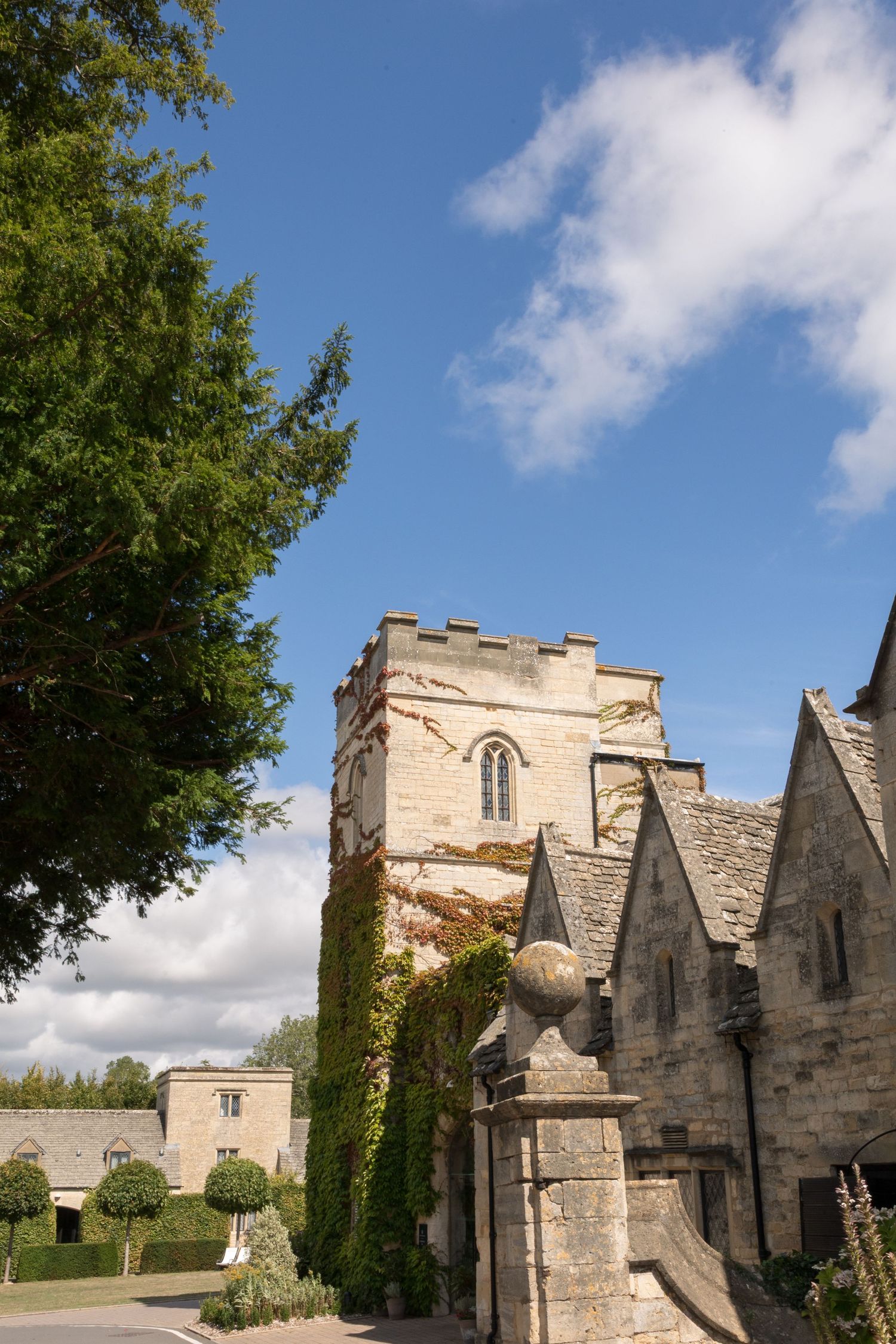 Historic stone church tower with battlements, ivy-covered walls, and Gothic architecture under a blue sky in England.