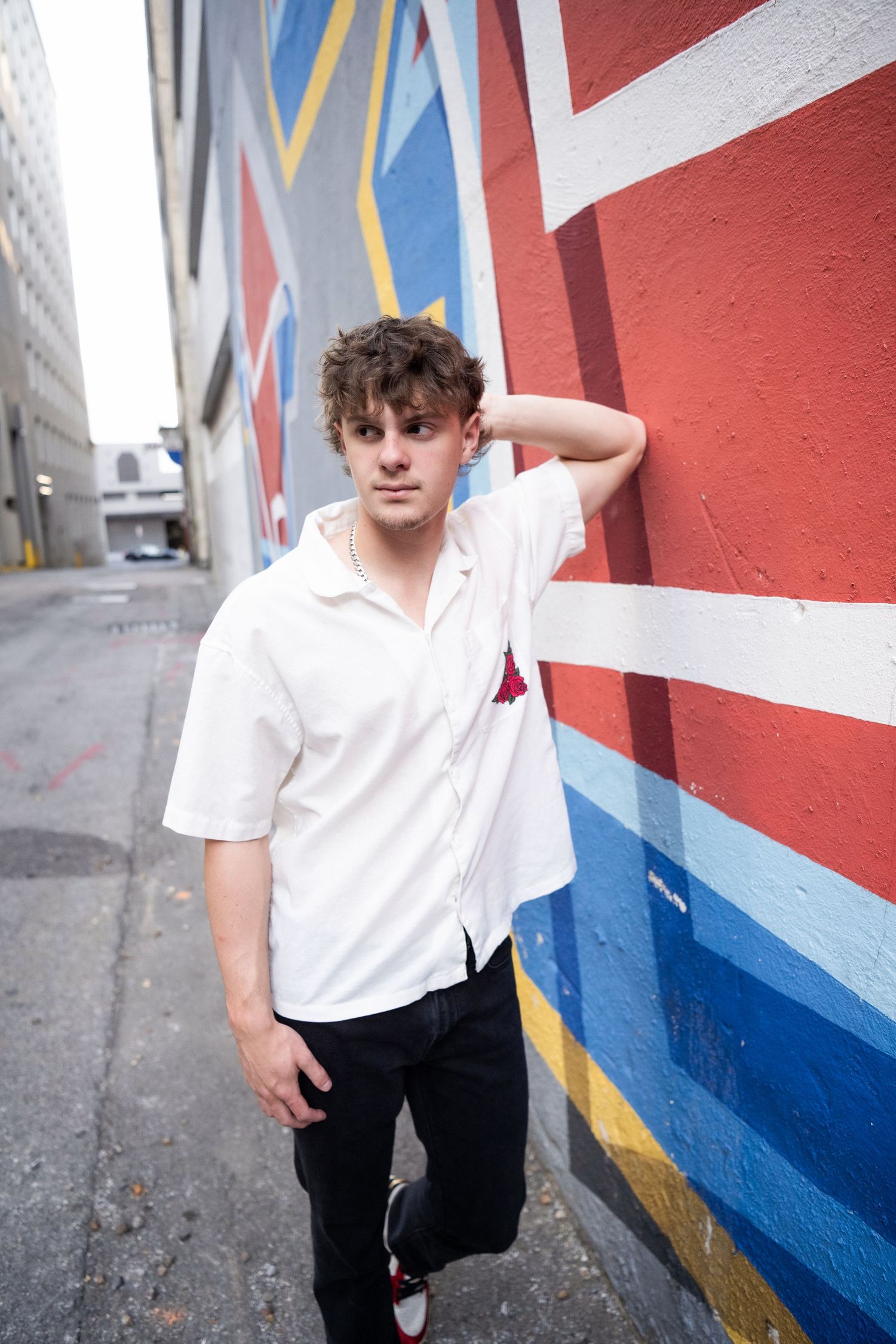 Young man in white shirt posing against colorful red and blue mural in urban alley.