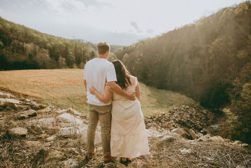 Couple embracing while overlooking a scenic mountain valley landscape in warm golden sunlight.