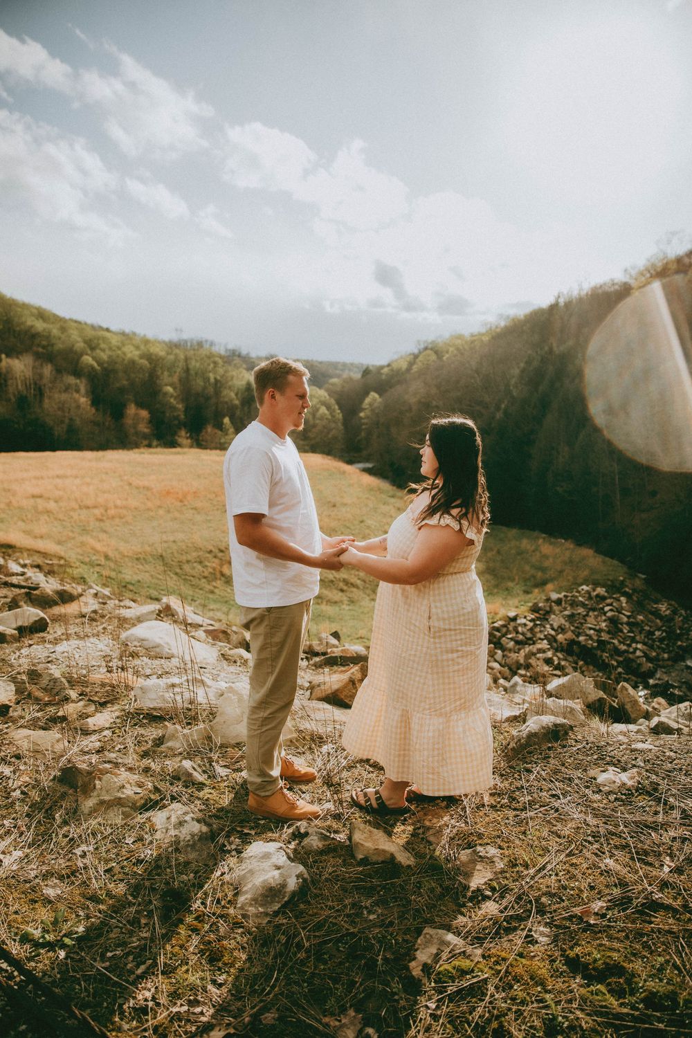 Couple holding hands on rocky hillside with scenic mountain valley and blue sky backdrop. indiana pa photographer