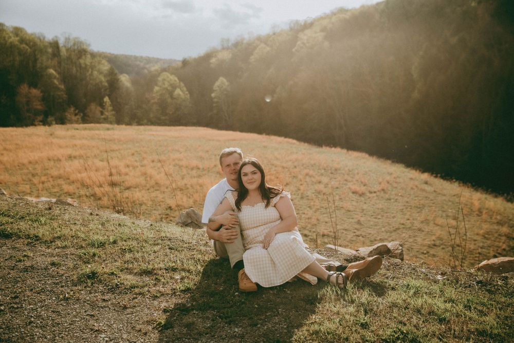 A couple poses outdoors on rocky terrain, woman in floral dress with baby bump, man in white tee, scenic valley. indiana pa photographer