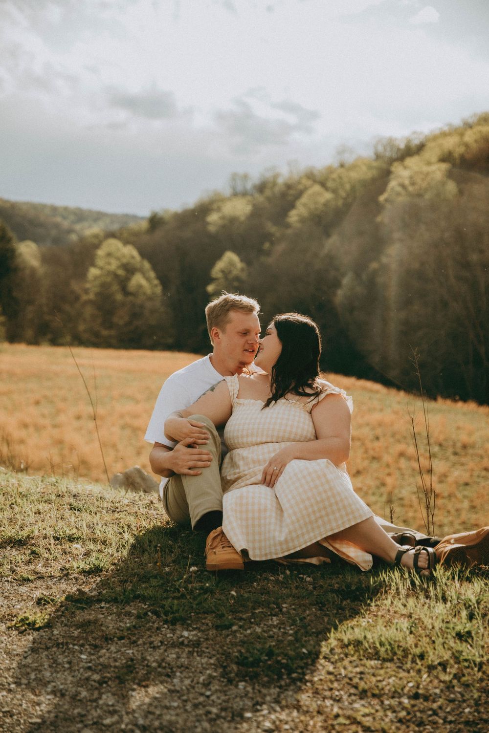 A couple poses outdoors on rocky terrain, woman in floral dress with baby bump, man in white tee, scenic valley. indiana pa photographer