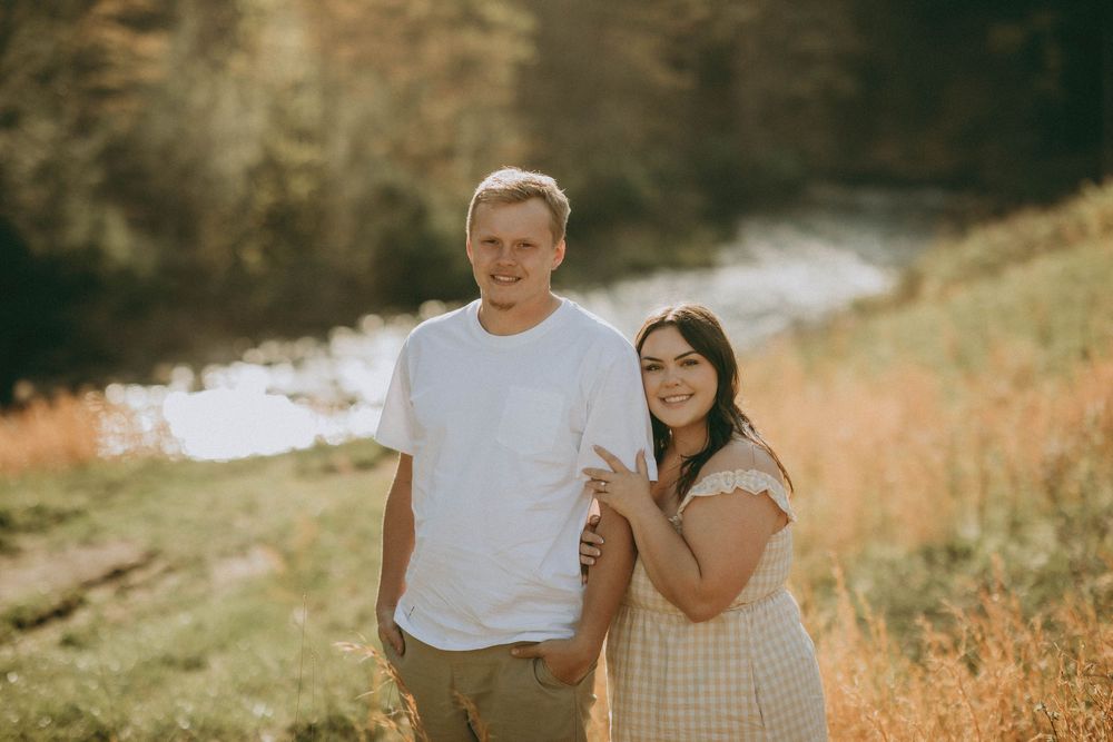 A couple poses outdoors on rocky terrain, woman in floral dress with baby bump, man in white tee, scenic valley. indiana pa photographer