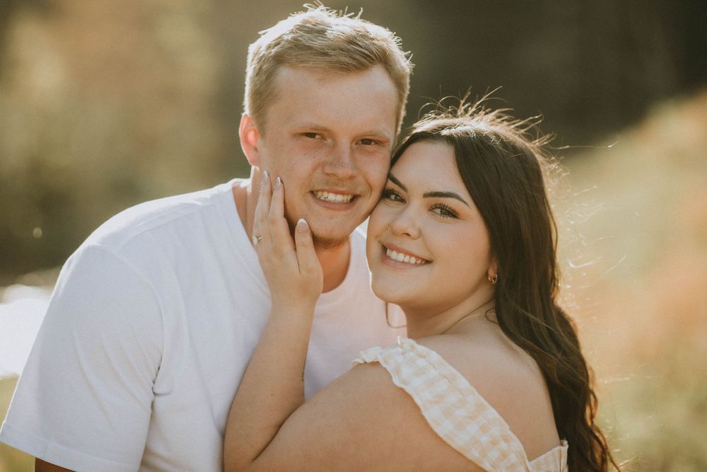 A couple poses outdoors on rocky terrain, woman in floral dress with baby bump, man in white tee, scenic valley. indiana pa photographer